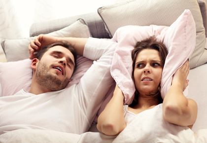 Man snoring during sleep and woman covering her ears with the pillow